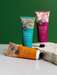 Three tubes of hand cream with different scents are displayed on a white surface against a green background.