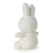 A white, fluffy stuffed bunny toy is sitting on its back with its arms outstretched.
