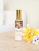 A bottle of "Native Frangipani & Peach Blossom" perfume with a gold cap, placed on a table next to a bunch of yellow flowers.