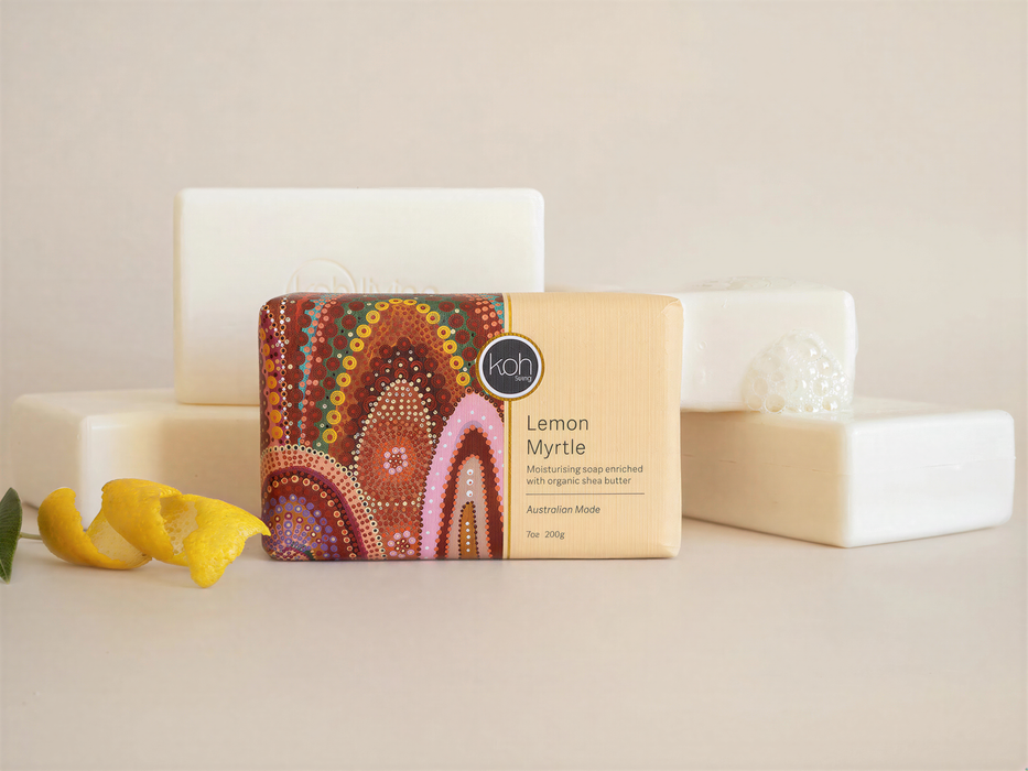 A rectangular bar of soap with a colorful, abstract design on it, placed on a white surface next to a lemon peel and a white rectangular object.
