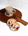 A wooden serving board holds a white mug filled with a beverage, accompanied by two coasters with a floral design.