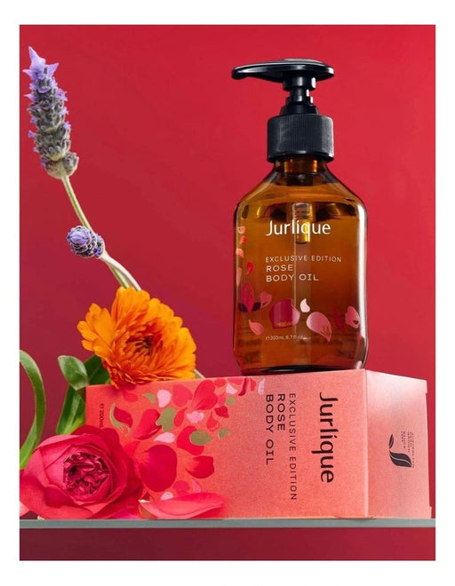 a bottle of Jurlique exclusive edition rose body oil, surrounded by a bouquet of flowers and a pink box with the same product name.