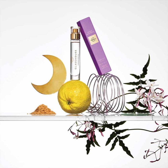a collection of various objects, including a crescent moon, a bottle of perfume, a lemon, a wire coiled object, and some flowers, all arranged on a shelf.
