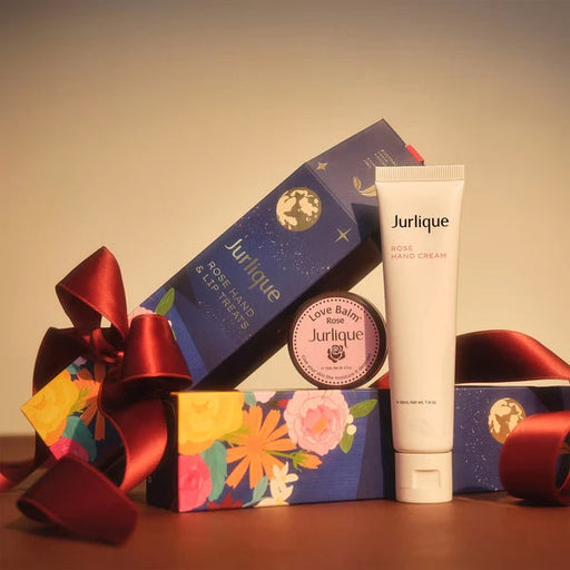 a collection of beauty products, including a tube of Jurique Rose Hand Cream, a box of Jurique Rose Hand Cream, and a small round container of Jurique Love Balm. The products are arranged on a surface with a red ribbon, creating a visually appealing display.
