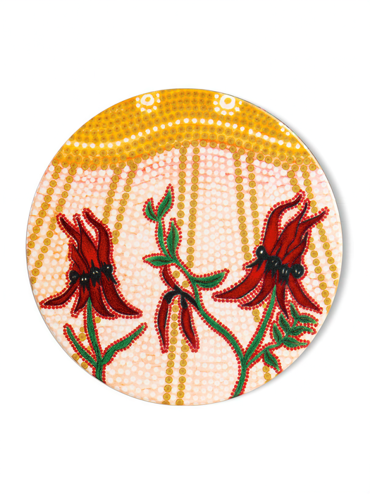 The image is a circular plate with a vibrant floral design featuring red flowers and green leaves against a yellow background with white dots.