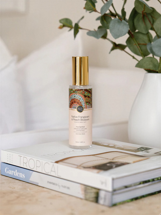 A bottle of "Native Franciscan & Peach Blossom" perfume is placed on top of a stack of books, with a potted plant visible in the background.