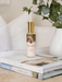 A bottle of "Native Franciscan & Peach Blossom" perfume is placed on top of a stack of books, with a potted plant visible in the background.