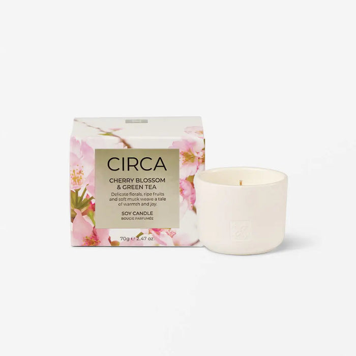 a white ceramic candle in a box with a floral design, and a small white candle next to it.