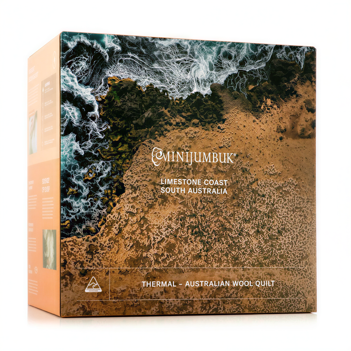 The image is a box for a thermal Australian wool quilt, featuring a landscape with a rocky coastline and ocean waves.
