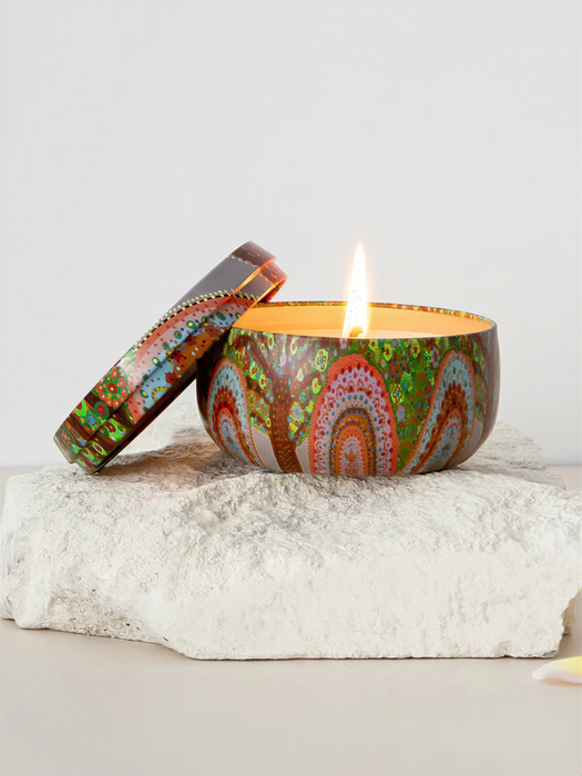 A colorful ceramic candle holder with a lit candle sits on a white rock, creating a warm and inviting atmosphere.