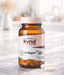 A bottle of Kynd Collagen 180 capsules is placed on a marble countertop, with a blurred background.