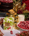 a table with a variety of items, including a box of CIRCA raspberry-flavored tea, a bowl of raspberries, a candle, and a cake. The table is decorated with gold and red ornaments, and the overall scene appears to be a festive or holiday-themed setting.
