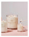 Three large glass jars with lit candles, each labeled with the "GLASSHOUSE Fragrances" logo, placed on a pink background.
