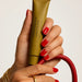 A person's hand holding a tube of lotion with red nail polish, and a red purse or bag is visible in the background.