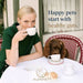 A woman in a green dress is sitting at a table with a brown dog, both enjoying tea together.