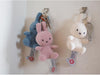 Three small stuffed bunny keychains hanging on a wall, each with a key attached to it.