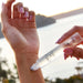 A person's hand applying a product to their wrist, with a body of water and a sunset in the background.