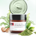 a jar of Swiss Skin Care's anti-pollution clay mask, surrounded by green leaves and a pile of the clay powder.