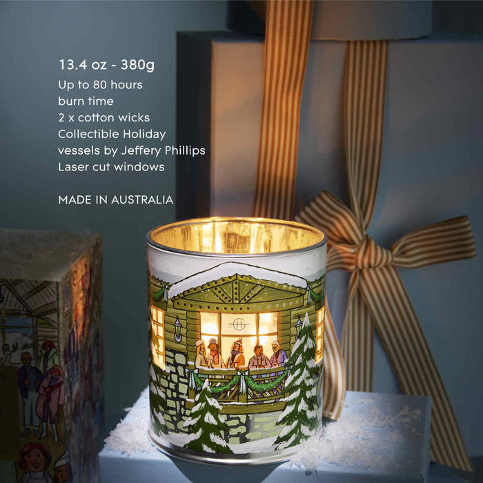 A candle in a white container with a winter scene design, placed on a table with a striped ribbon.