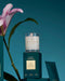 a white candle labeled "Glasshouse" on a green box, with a pink flower and a green leaf in the background.