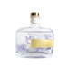 A clear glass bottle with a gold cap, containing a transparent liquid and decorated with purple flowers. The bottle has a yellow label that reads "BLUEOCAR HOME Fragrance Diffuser".