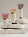Three tubes of hand cream with different scents and colors are displayed on a stack of white rocks.