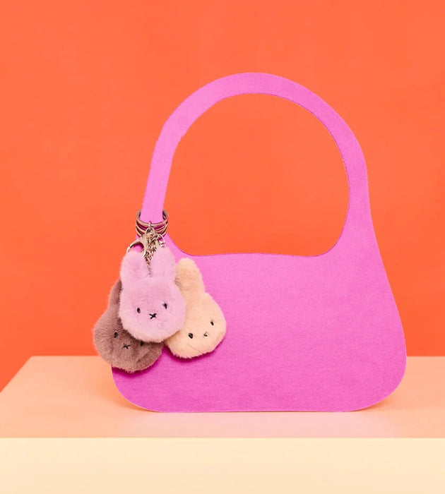 A pink handbag with three small, plush bunny keychains attached to it.