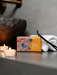 a bar of soap with a bird design, placed on a counter next to a white towel and a pair of black scissors. There are also two lit candles in the background.