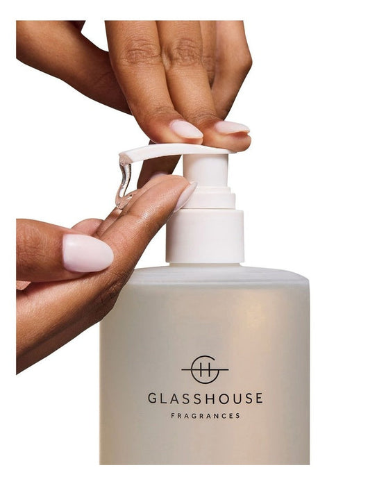 A person's hands applying a liquid product from a pump bottle labeled "GLASSHOUSE FRAGRANCES".