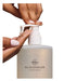 A person's hands applying a liquid product from a pump bottle labeled "GLASSHOUSE FRAGRANCES".