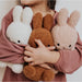 A child is holding three stuffed rabbits in their arms, wearing a pink sweater.