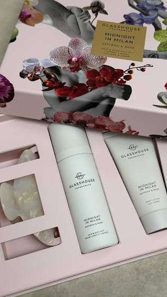 A gift set from the brand "GLASSHOUSE" containing two products, one cream and one body wash, presented in a pink box with a floral design.