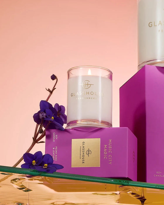 a collection of purple and pink boxes, a white candle, and purple flowers, all arranged on a reflective surface.