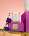 a collection of purple and pink boxes, a white candle, and purple flowers, all arranged on a reflective surface.