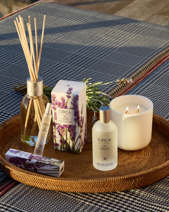 a collection of various scented products, including a candle, a diffuser, and a bottle, arranged on a woven tray.