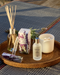 a collection of various scented products, including a candle, a diffuser, and a bottle, arranged on a woven tray.
