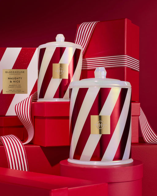 two large, striped candles with a red and white color scheme, placed on a red surface. The candles appear to be part of a holiday-themed collection, as suggested by the red and white striped boxes and the red background.
