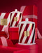 two large, striped candles with a red and white color scheme, placed on a red surface. The candles appear to be part of a holiday-themed collection, as suggested by the red and white striped boxes and the red background.