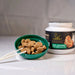 a green bowl filled with dog treats next to a white jar of pet food, with a pair of white chopsticks placed in the bowl.
