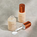two bottles of Syrene Black Pearl Illuminating Serum, with one bottle open and the other one closed, both containing a white substance.