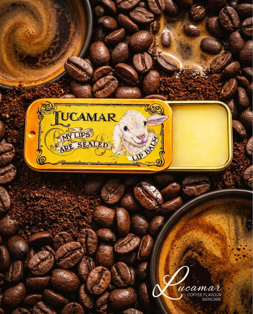 a yellow tin of Lucamar lip balm surrounded by coffee beans and a cup of coffee.