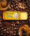 a yellow tin of Lucamar lip balm surrounded by coffee beans and a cup of coffee.