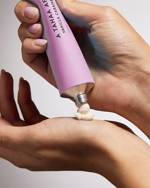 A hand is applying a pink tube of cream to a person's hand.