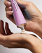 A hand is applying a pink tube of cream to a person's hand.