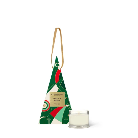 A triangular-shaped box with a gold label and a small white candle in a glass holder are displayed against a white background.