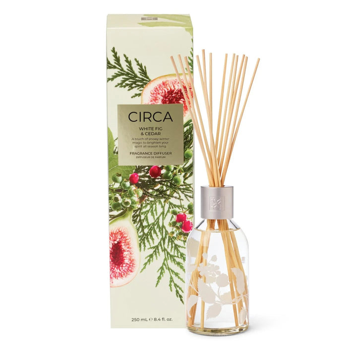 a white box with a design of pine branches and pine cones, and a clear glass vase with wooden sticks inside, both placed next to each other.