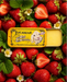 a tin of Lucamar lip balm surrounded by fresh strawberries and leaves.