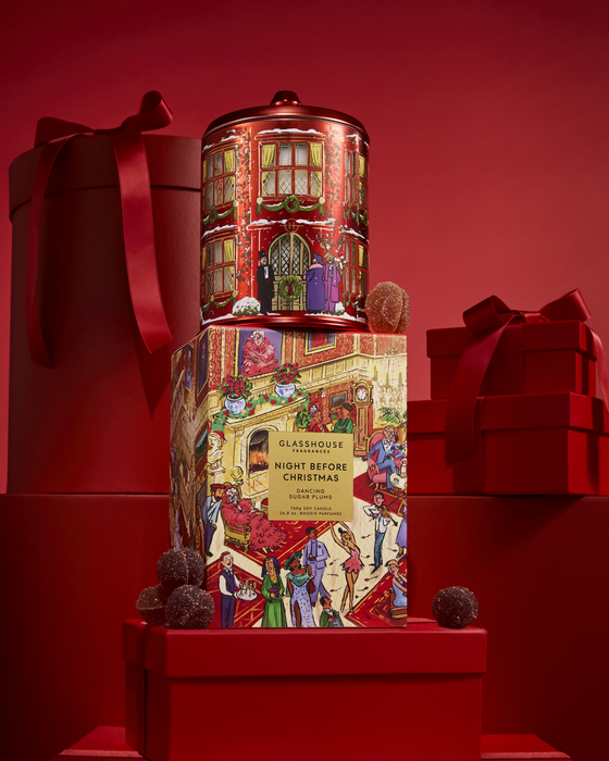 a red gift box with a picture of a building and people, along with the text "GLASSHOUSE NIGHT BEFORE CHRISTMAS DANDELION" and "DANDELION SUGAR FREE". The box is placed on top of a stack of red gift boxes, and there are also some small red balls around the box.