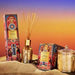 a collection of decorative items, including a box of incense sticks, a glass jar, and a small vase, all placed on a sandy surface against a colorful sunset background.