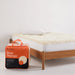 An orange and black box labeled "SLEEP THERAPY" is placed next to a wooden bed frame with a white mattress and a white pillow.